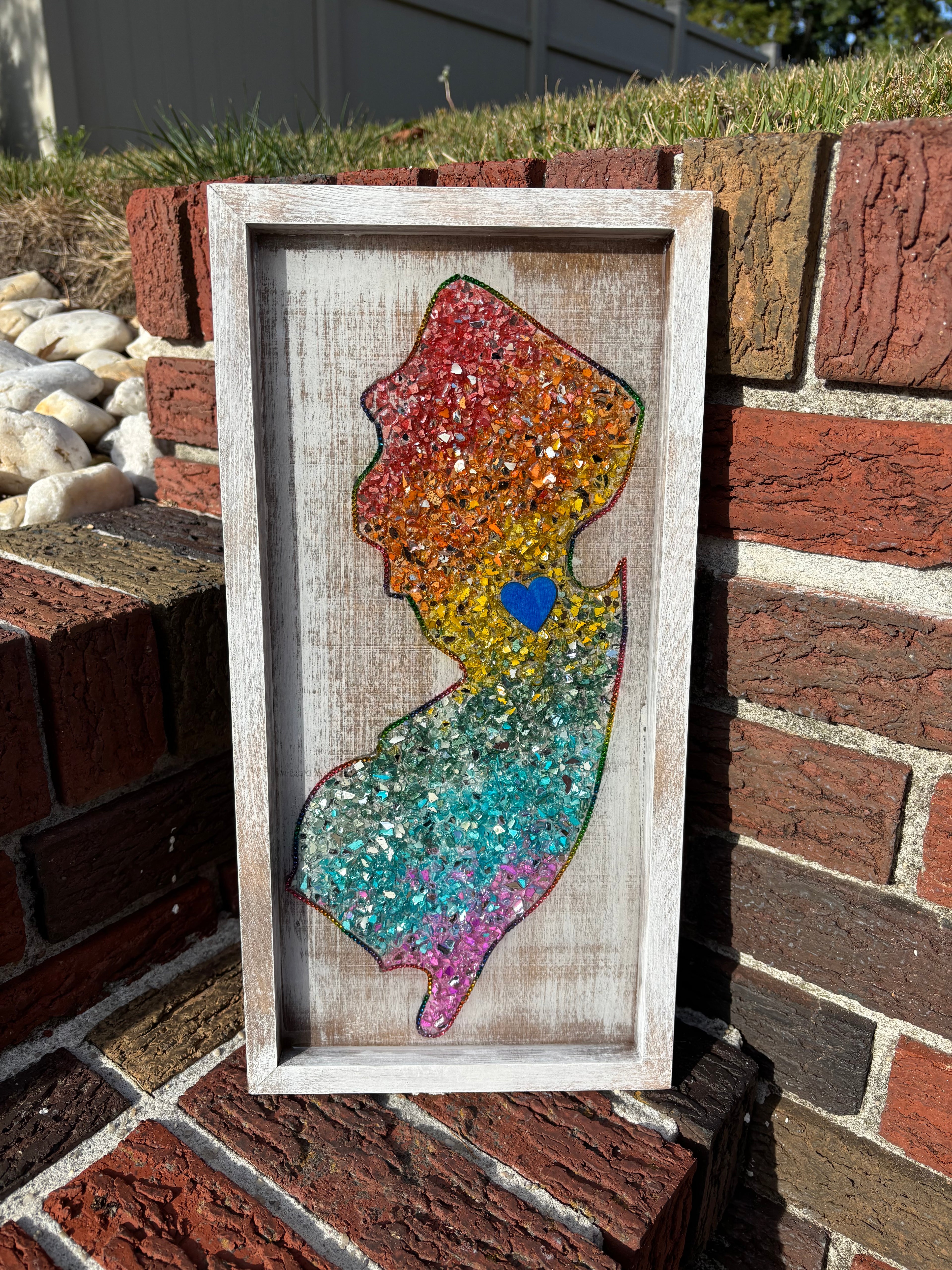 Colorful New Jersey art piece in a wooden frame on a brick wall.