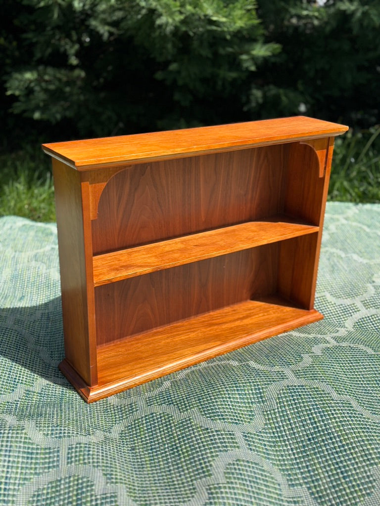 Wooden bookshelf on a green outdoor surface with blurred natural background