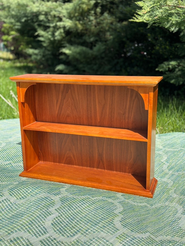 Wooden bookshelf outdoors on a green surface with trees in the background