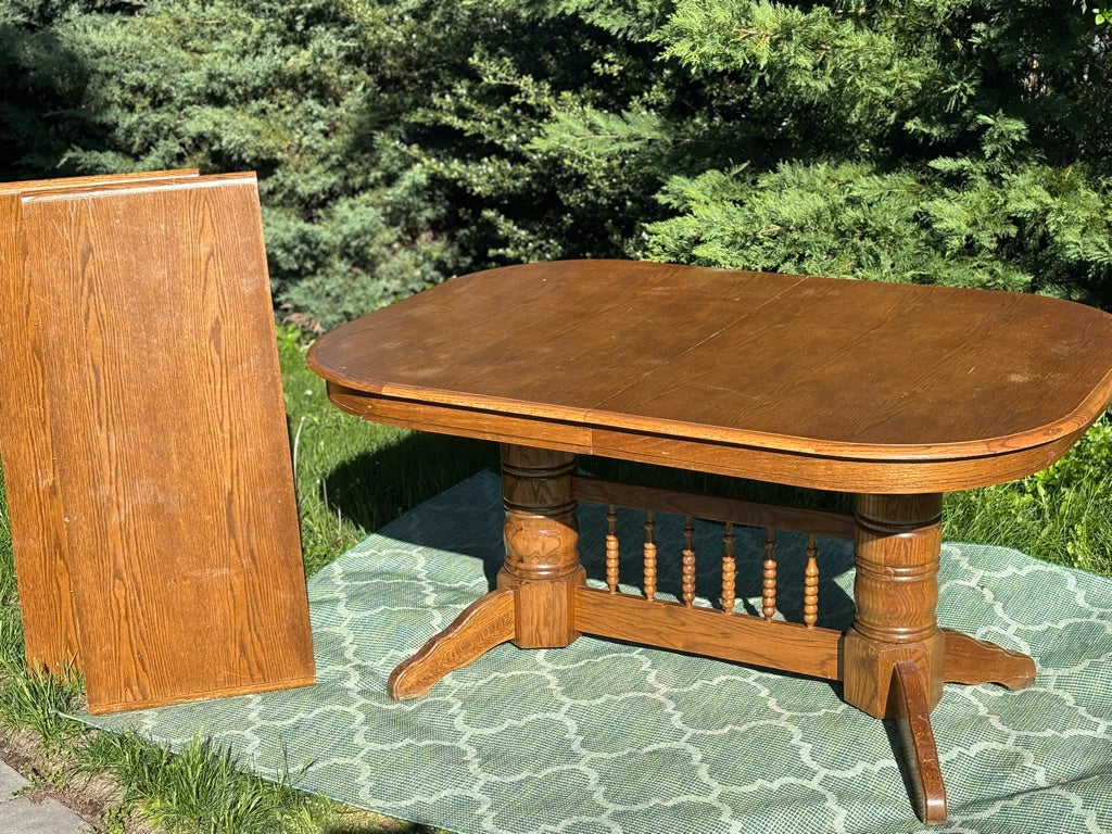 Wooden dining table with a leaf on a green patterned rug outdoors.