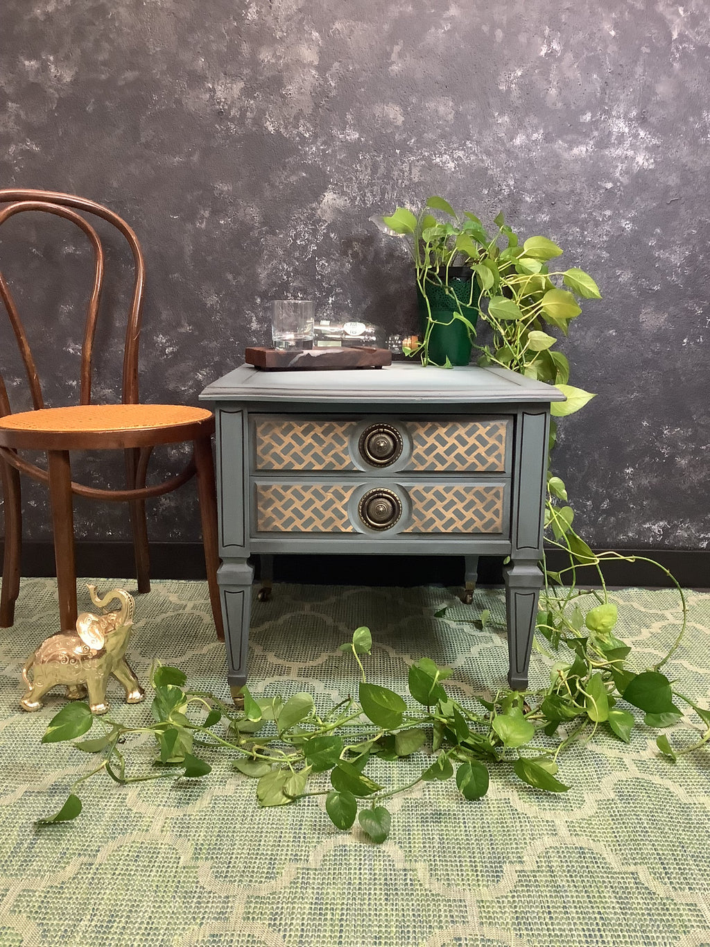 Small gray side table with decorative items against a dark textured wall.