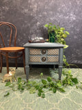Small gray side table with decorative items against a dark textured wall.