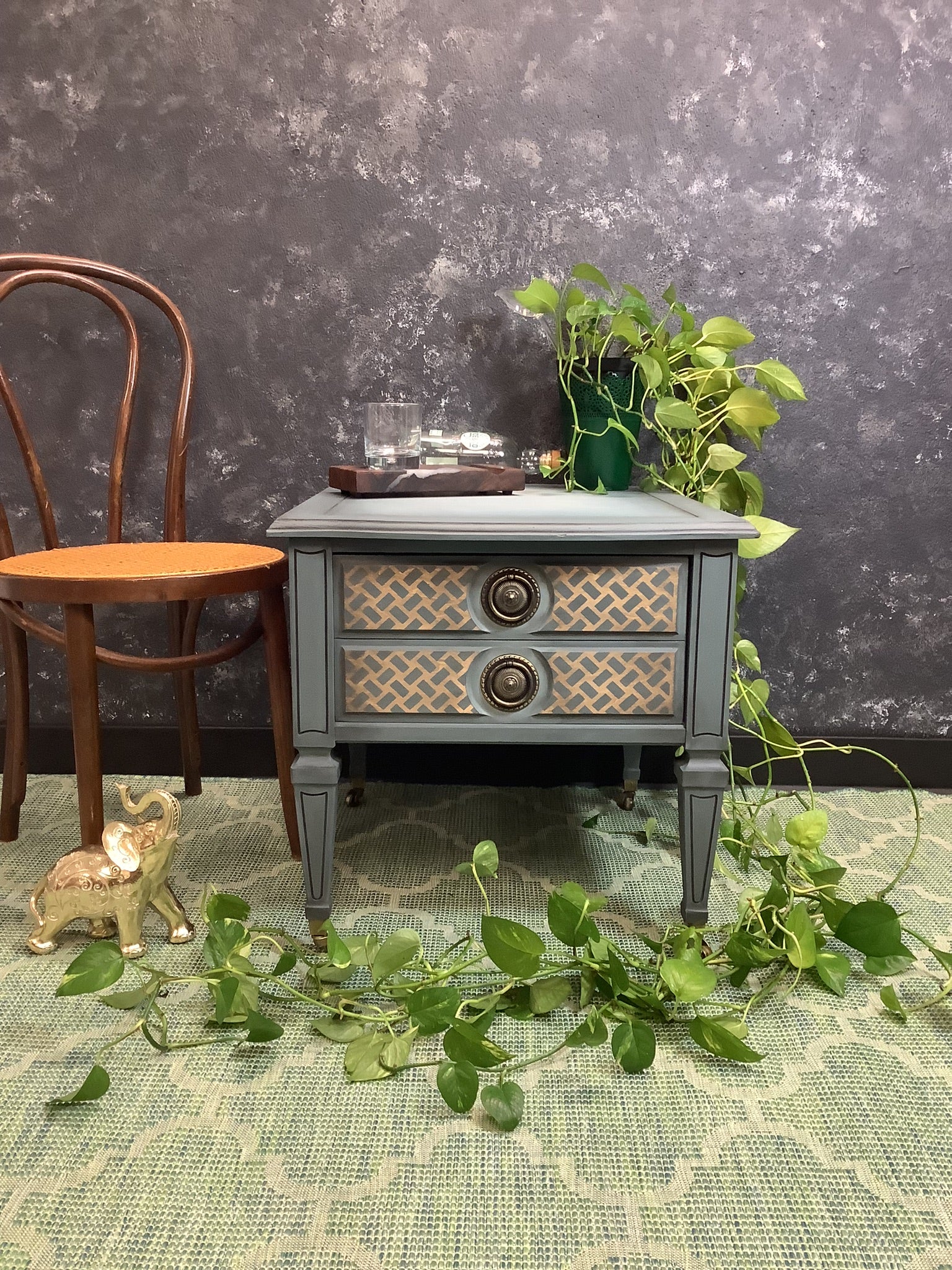 Small gray side table with decorative items against a dark textured wall.