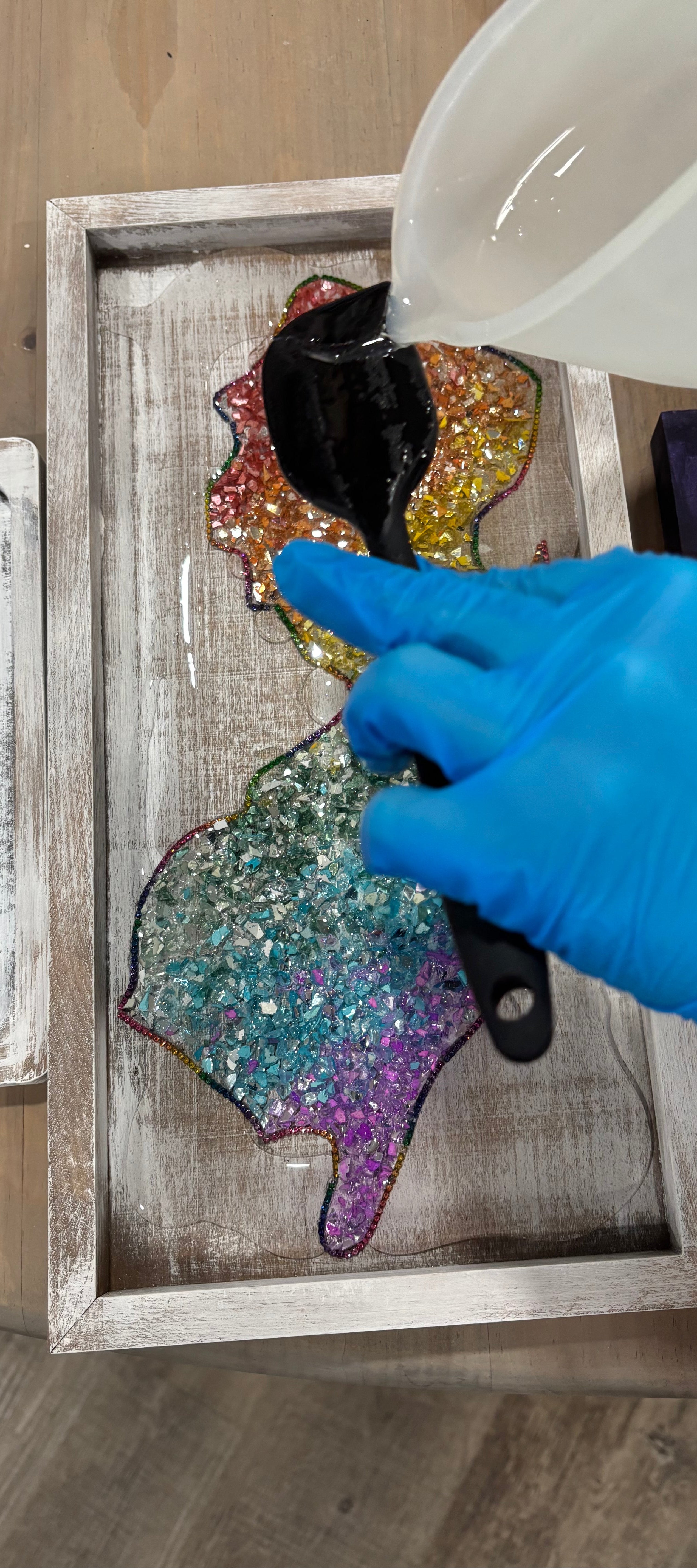 Hand applying a clear resin to a wooden frame with a gloved hand.