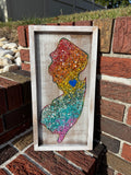 Colorful New Jersey art piece in a wooden frame on a brick wall.
