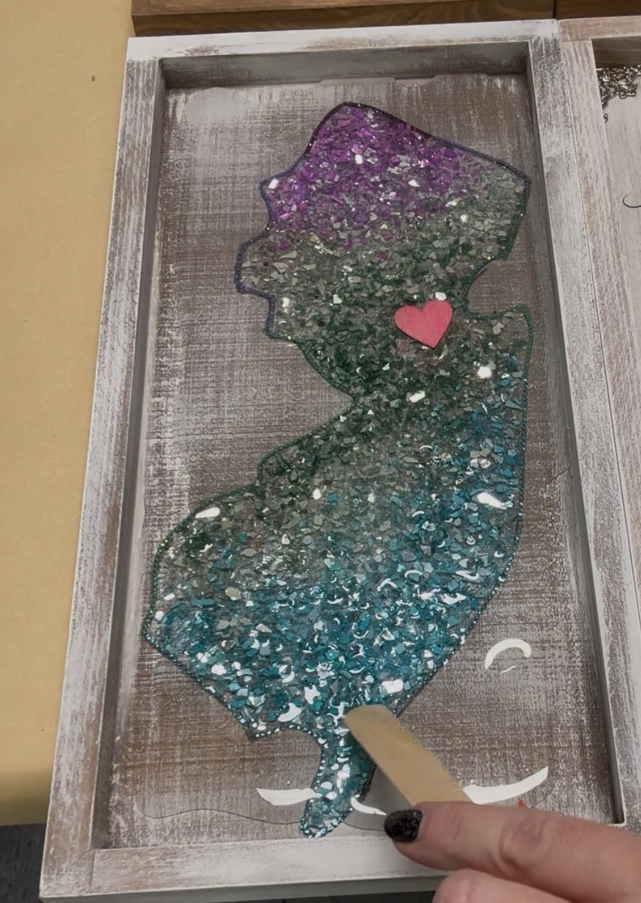 Decorative piece of New Jersey with crushed glass and heart, framed in wooden border.
